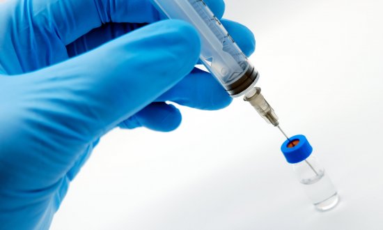 Gloved hand holding syringe inserted into small vial
