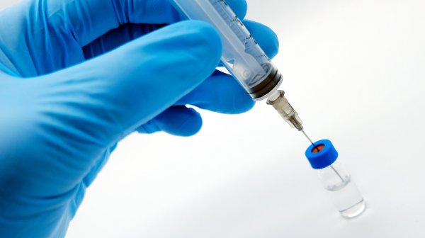 Gloved hand holding syringe inserted into small vial
