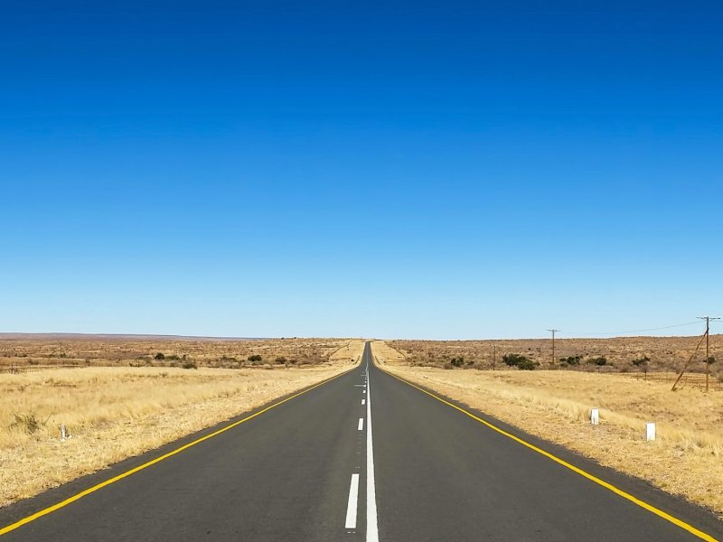 Photo of road against clear blue sky and dry brush